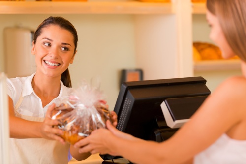 Please enjoy! Beautiful young female baker giving cookies to customer and smiling
